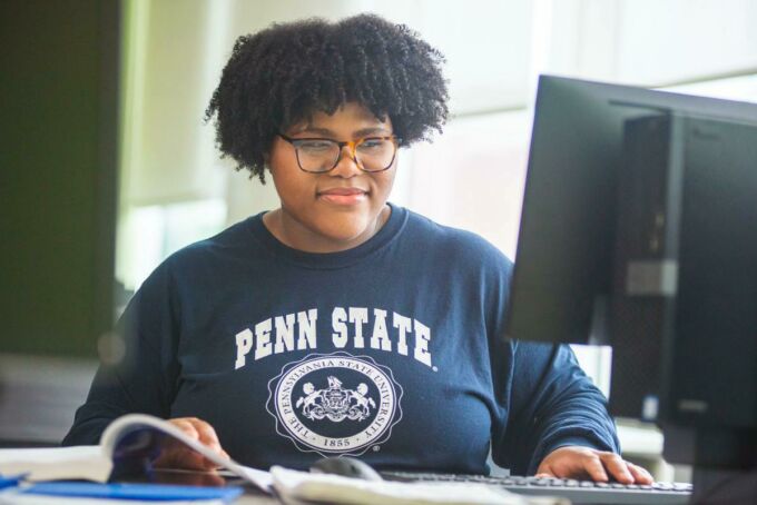 student in Penn State shirt at computer with book and notebook