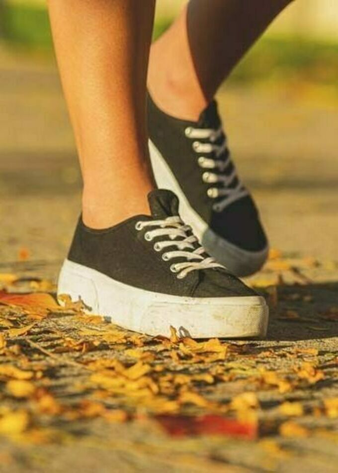 Close-up of female feet in black canvas sneakers on an autumn sidewalk.
