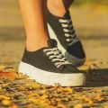 Close-up of female feet in black canvas sneakers on an autumn sidewalk.