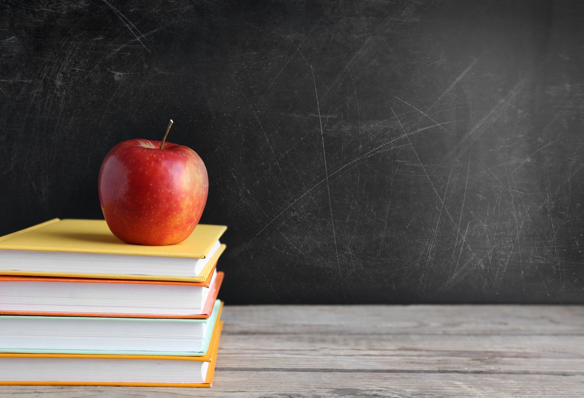 Red apple on a stack of books in front of a black chalkboard.